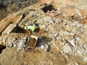 Archeologi scavano diligentemente i resti di un edificio di tarda epoca romana. Parte del muro può essere visto sulla sinistra mentre pezzi del pavimento in pietra sopravvivono sulla destra. Credit: University of Leicester