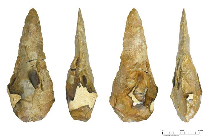  Photograph of the largest giant handaxe taken from four different angles. It is roughly teardrop shaped with a point at one end and a flatter curve at the other. It is made of an orangey yellow stone.