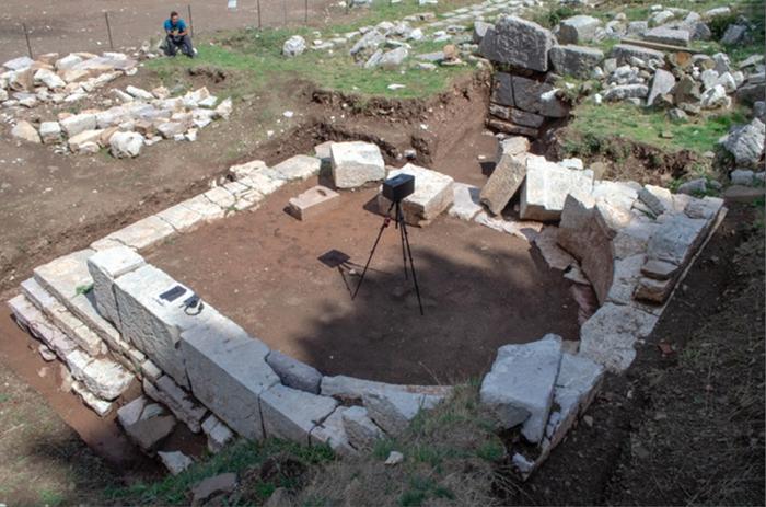 Excavated building with semi-circular interior stone wall, speaker placed at focal point of curve. Credits: Image by Pamela Jordan