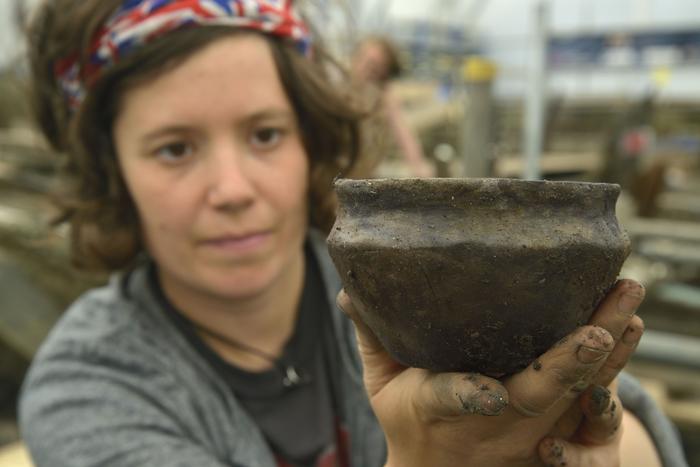 A member of the Cambridge Archaeological Unit on site at the Must Farm excavation in 2016 displays a pot recovered from the 'kitchen area' of one of the roundhouses.  