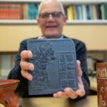 University of Cincinnati Professor David Lentz holds up a reproduction tile featuring ancient Maya glyphs. Researchers discovered evidence of ceremonial offerings at the site of an ancient Maya ballcourt in Yaxnohcah, Mexico. Credits: Andrew Higley