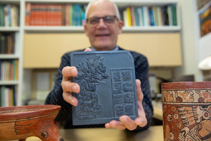 University of Cincinnati Professor David Lentz holds up a reproduction tile featuring ancient Maya glyphs. Researchers discovered evidence of ceremonial offerings at the site of an ancient Maya ballcourt in Yaxnohcah, Mexico. Credits: Andrew Higley